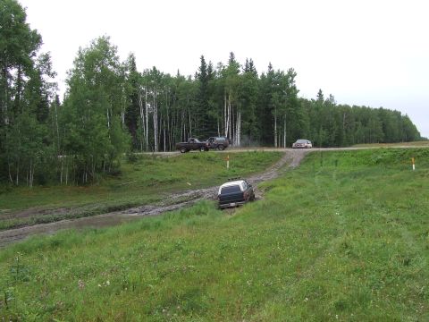1988 Ford Bronco - Several vehicles navigate a dirt track and grassy terrain with a forest backdrop.