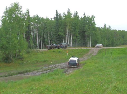 1988 Ford Bronco - Multiple vehicles navigate a muddy road through a wooded area.