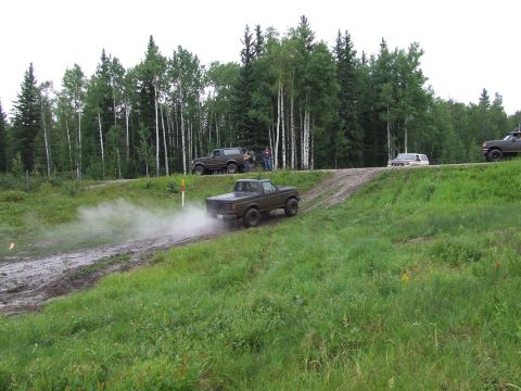 1988 Ford Bronco - Several vehicles navigate a muddy track surrounded by trees.
