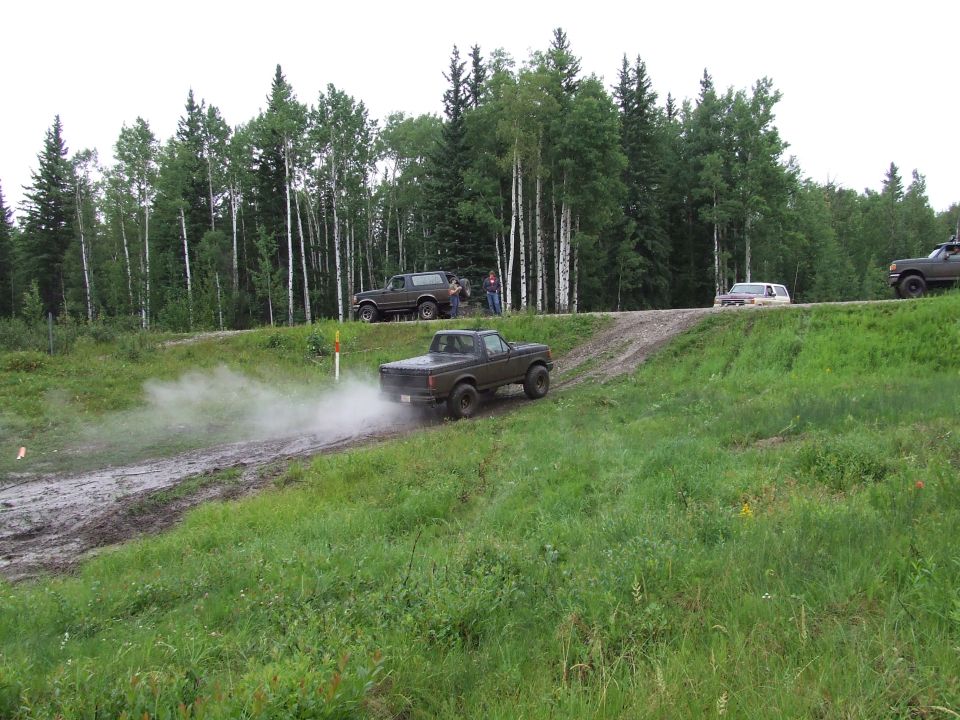 Brown 1987 Ford Bronco driving on a dirt road, kicking up dust