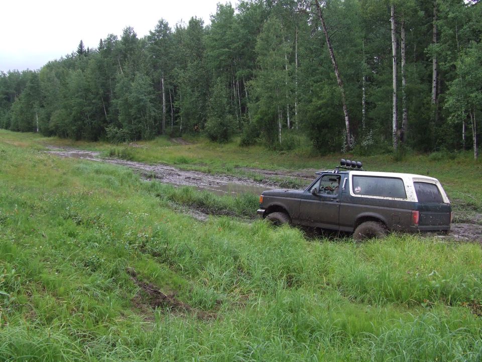 Dark green and white SUV stuck in mud, roof rack with lights, 1987 model