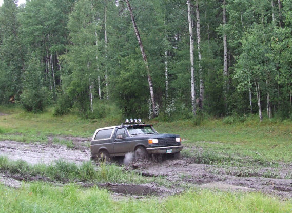 Ford Bronco driving through a muddy trail in a wooded area