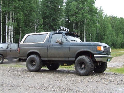 1988 Ford Bronco - This lifted SUV, likely a 1992-1996 Ford Bronco, is shown in a three-quarter front view with off-road tires and auxiliary lights.