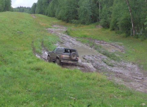 1988 Ford Bronco - A Ford Bronco navigates a muddy track on a green, wooded hillside.
