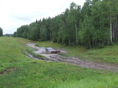 1988 Ford Bronco - A dark SUV navigates a muddy track through a wooded area.