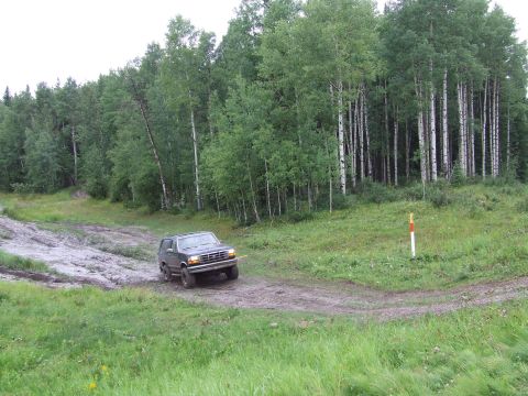 1988 Ford Bronco - A Ford Bronco drives through a muddy track surrounded by a forest.