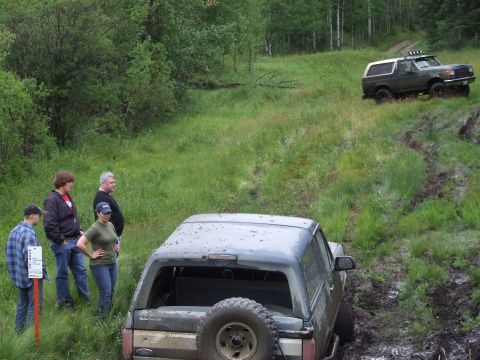 1988 Ford Bronco - Two Ford Broncos navigate a muddy off-road course with onlookers.