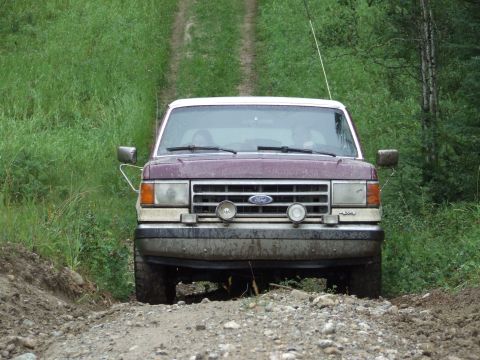 1988 Ford Bronco - Front view of a 1988 Ford Bronco driving on a dirt road through a wooded area.