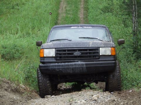 1988 Ford Bronco - A black Ford Bronco navigates a rough dirt path surrounded by greenery.