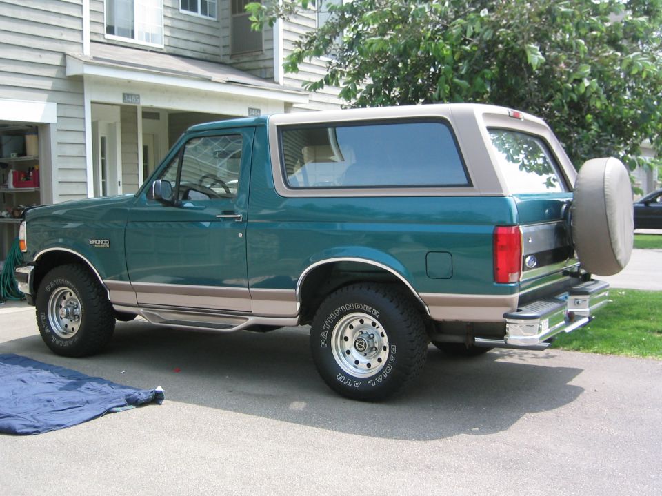 Teal and tan Ford Bronco SUV, rear side view, parked in driveway with spare tire on tailgate