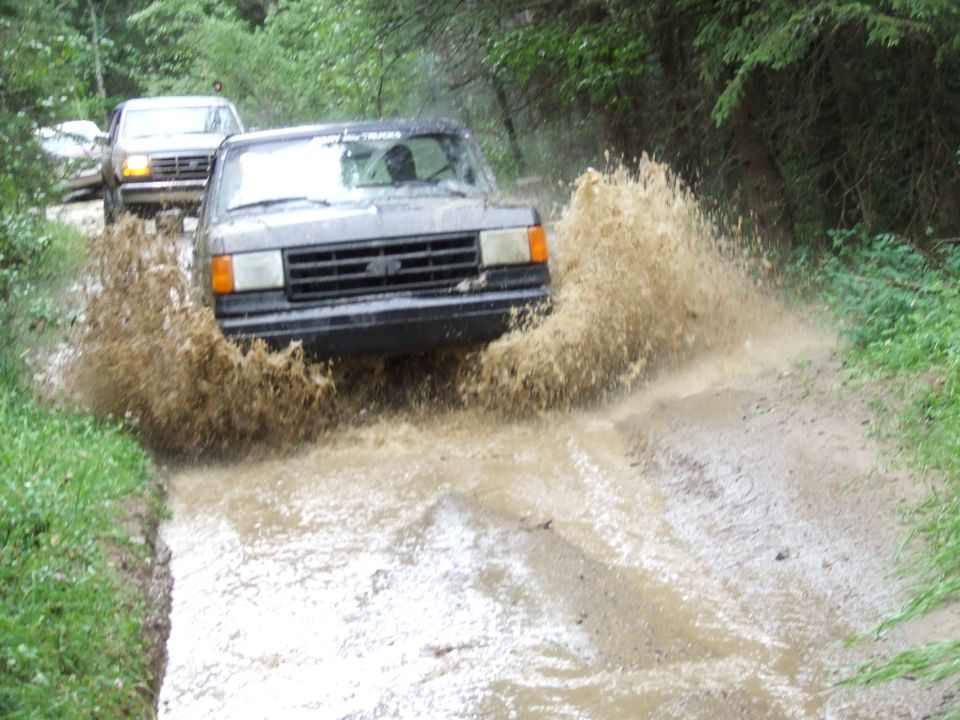 Dark SUV splashing through mud puddle, another SUV behind it