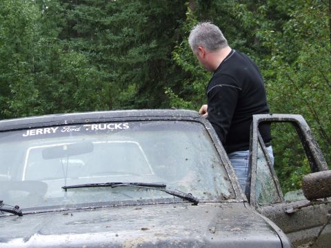 1988 Ford Bronco - Man leans on a muddy 1988 Ford Bronco, which has a 'JERRY Ford TRUCKS' decal on the windshield.