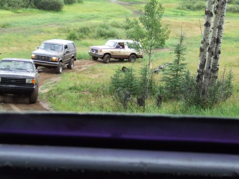 1988 Ford Bronco - Three SUVs navigate a dirt path through a rural, green landscape with trees and hills.