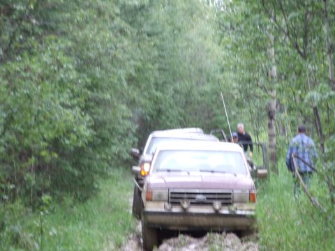 1988 Ford Bronco - Two SUVs navigate a muddy, wooded trail during an off-road excursion.