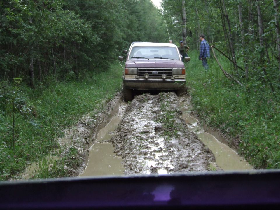 1988 Ford Bronco navigating a muddy trail with trees on either side