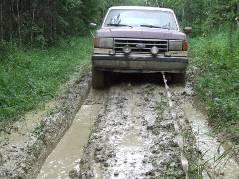 1988 Ford Bronco - A Ford Bronco navigates a challenging muddy trail, its front end partially submerged in water.