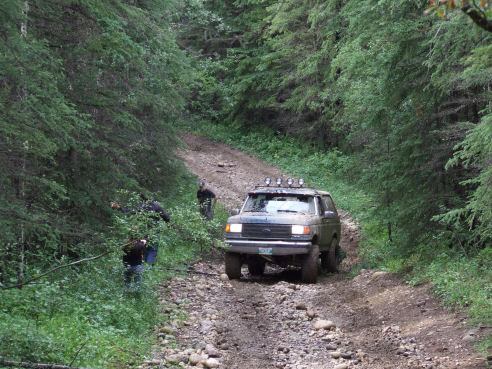 1988 Ford Bronco driving on a rocky, wooded dirt road