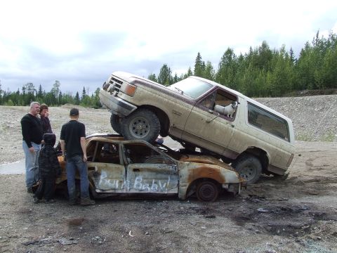 1988 Ford Bronco - A 1988 Ford Bronco is parked on top of a burnt-out car. Text on the car reads 'Burn Baby!'