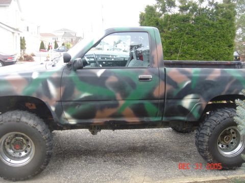 1992 Toyota Tacoma - This Toyota pickup truck, painted in camouflage, is viewed from the side and features a single cab and off-road tires.