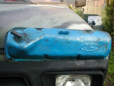 1979 Ford Bronco - A blue Ford valve cover is mounted on the hood of a vehicle, with the Ford emblem clearly visible.