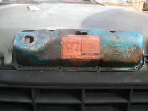 1979 Ford Bronco - A close-up of a worn valve cover with a Ford emblem and an emissions sticker.
