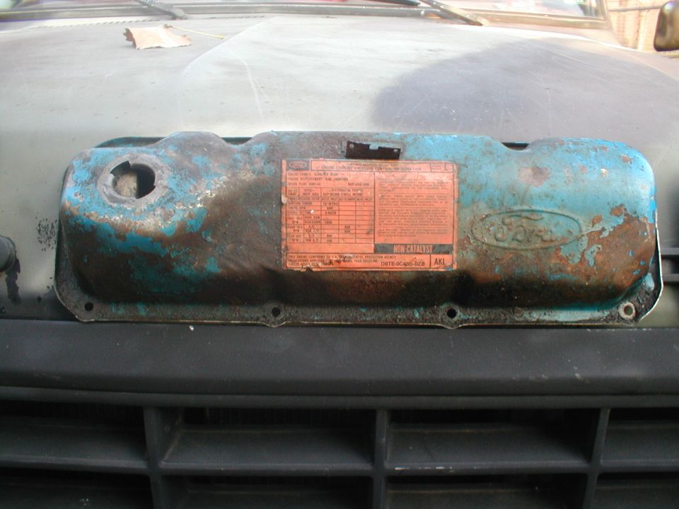 Rusty blue Ford valve cover with oval logo and orange emission control decal
