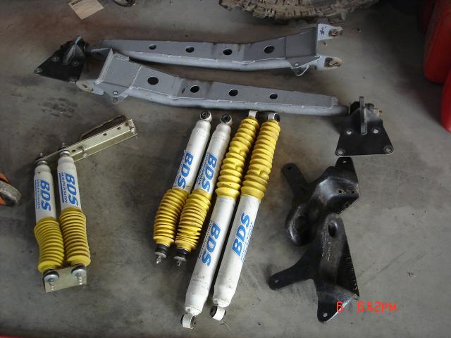 BDS shocks with yellow boots and gray metal suspension parts laid out on concrete floor