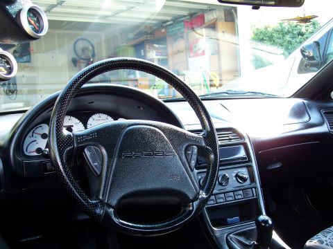 1995 Ford Probe - The interior of a car shows the steering wheel, dashboard, and aftermarket gauges mounted on the A-pillar.