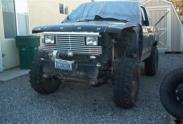 Black Ford Bronco with a tarp over the hood, missing front fender, and large tires