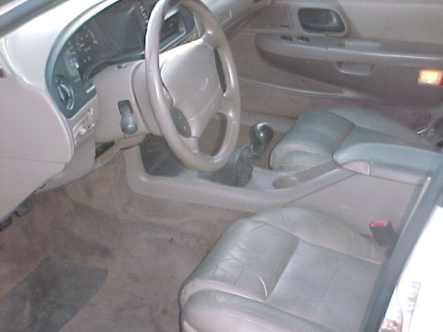 Tan leather interior of a 1995 Ford Taurus, showing the dashboard, steering wheel, center console with gear shifter, and front seats