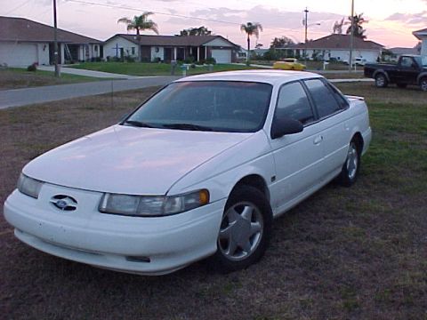 1994 Ford Taurus - A white 1994 Ford Taurus sedan is parked on a grassy area in front of a suburban house.