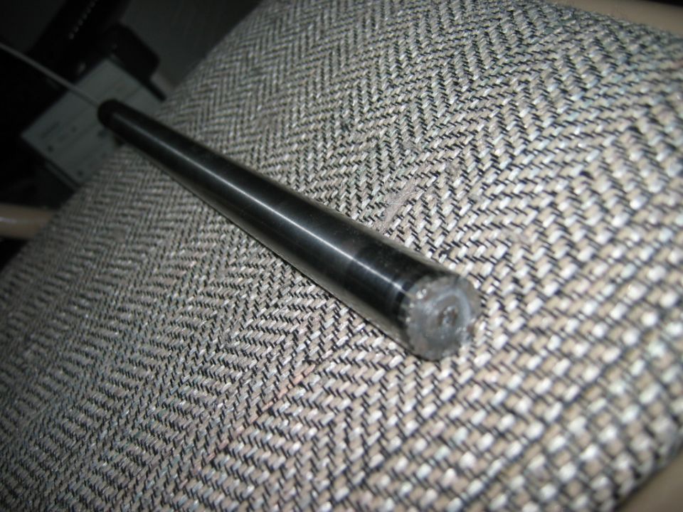Tapered dark metal shaft resting on gray tweed fabric