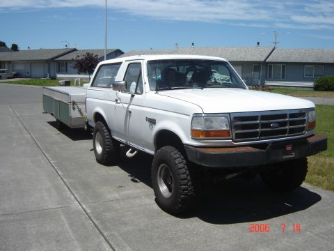 1993 Ford Bronco - White 1993 Ford Bronco with aftermarket bumper tows a trailer on a sunny day.