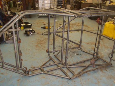 1978 Ford Bronco - Unfinished metal roll cage frame sits on a blue workshop floor with tools in the background.