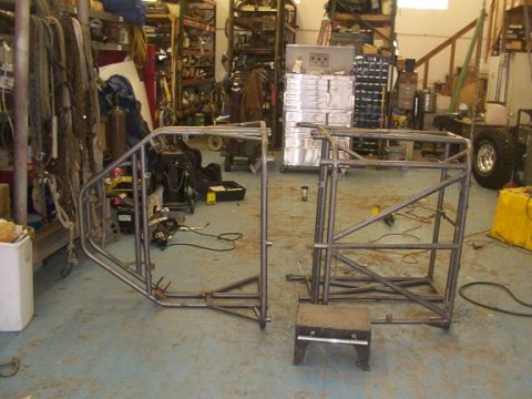 1978 Ford Bronco - Two sections of a custom-built roll cage frame are visible in a workshop setting, with tools and equipment in the background.