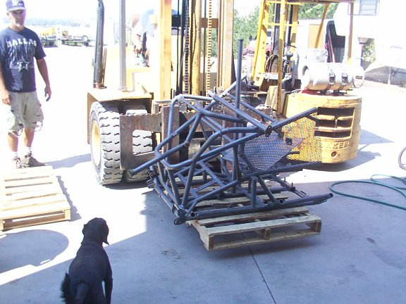 Roll cage assembly on wooden pallets, with a forklift and a man nearby