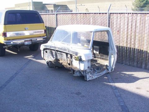 1978 Ford Bronco - A stripped-down white truck cab chassis sits on asphalt, with a yellow SUV parked behind it.