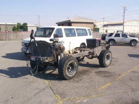 1978 Ford Bronco - A white van chassis sits on large tires, its engine exposed, in a parking lot with another vehicle visible.