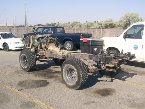 1978 Ford Bronco - A vehicle chassis, stripped down to its core components, sits in a parking lot with other vehicles in the background.