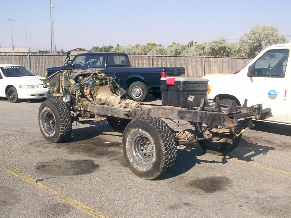 Vehicle chassis with engine and drivetrain, front 3/4 view. Multiple vehicles present