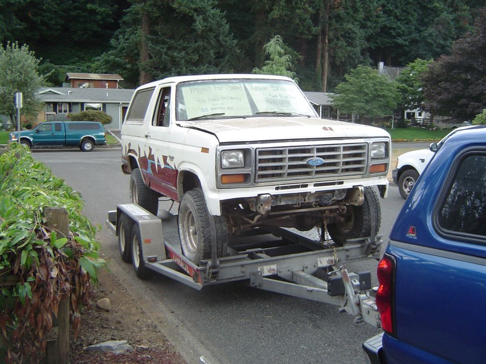 White Ford Bronco project on a trailer behind a blue truck
