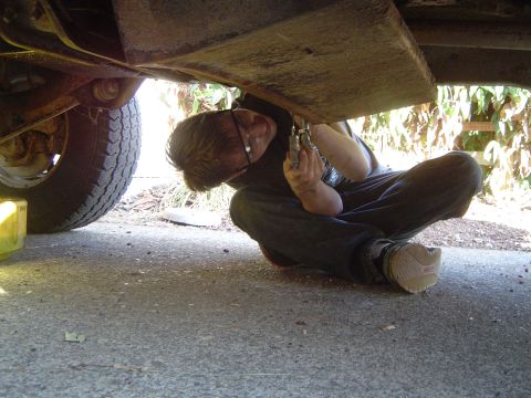 1972 Ford F-100 - A person is working on the underside of a vehicle, with a tire visible on the left side.