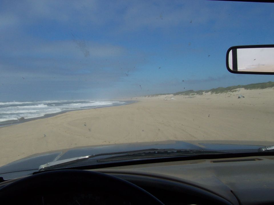 View from inside a vehicle driving on a sandy beach with ocean waves on the left