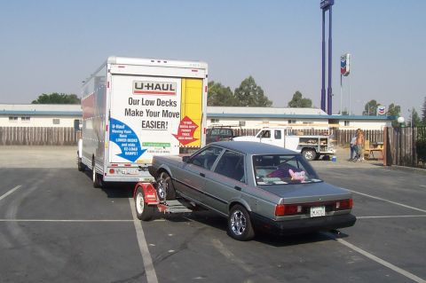 1994 Ford F-150 - A silver sedan is loaded onto a U-Haul trailer, with a U-Haul truck visible ahead.
