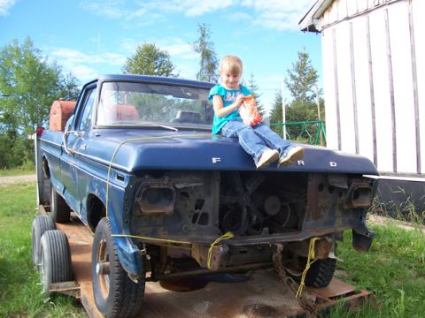 1996 Ford Bronco - A young girl sits on the hood of a blue Ford pickup truck being transported on a trailer.
