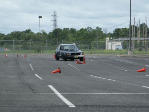 2001 Mercury Grand Marquis - A black hatchback navigates a cone course in an open parking lot under a cloudy sky.