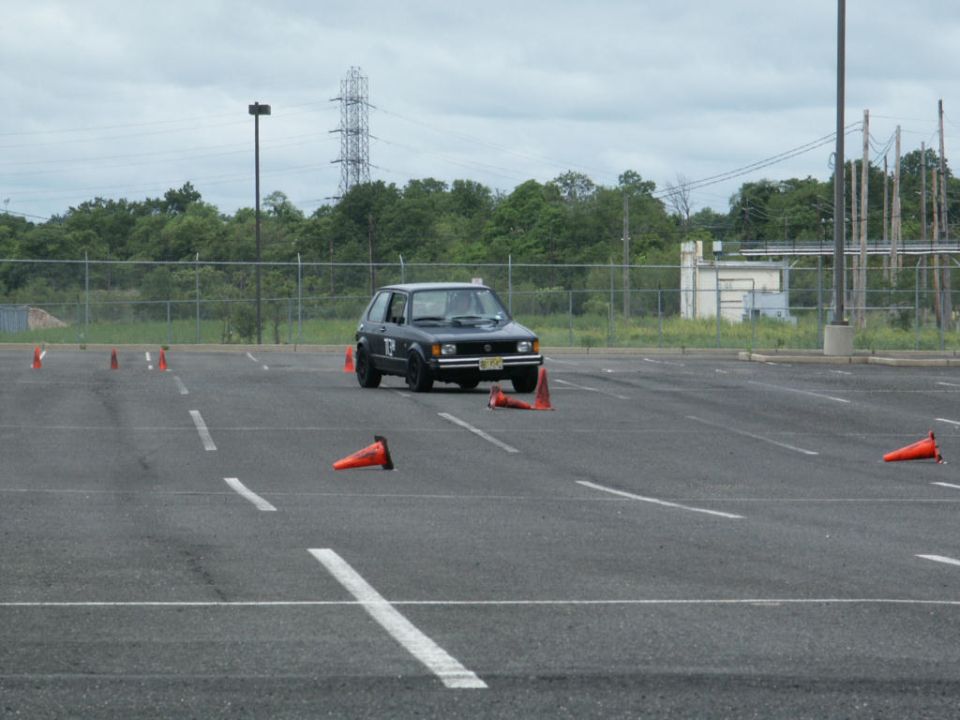 Black hatchback with number 12 on door driving through cones in a parking lot