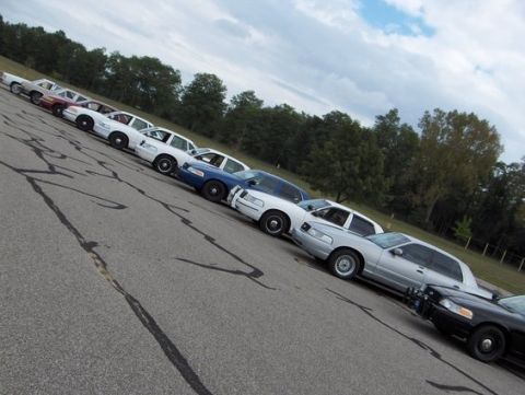 1988 Mercury Grand Marquis - A fleet of police cars are lined up on a paved lot under a cloudy sky.