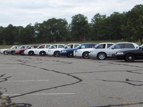 1988 Mercury Grand Marquis - Several police cars are parked in a lot under an overcast sky.