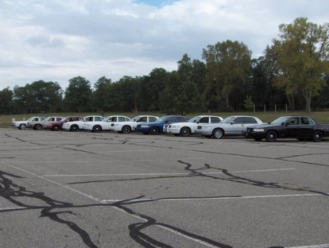 1988 Mercury Grand Marquis - A row of police cruisers and civilian sedans are parked in a lot, with several appearing to be from the late 1980s.